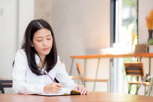 Beautiful business asian young woman writing on notebook on table, girl work at coffee shop, freelance business concept.