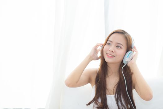 Beautiful asian young woman enjoy listen music with headphone while sitting in bedroom, relax girl with earphone internet online, leisure and technology concept.