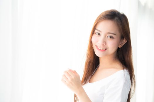 Beautiful young asian woman standing the window and smile while wake up with sunrise at morning, lifestyle and relax concept.