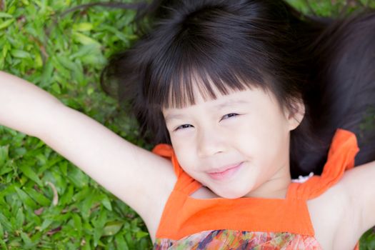 Beautiful portrait little girl asian of a smiling lying on green grass at the park, kid leisure and joyful in outdoor.