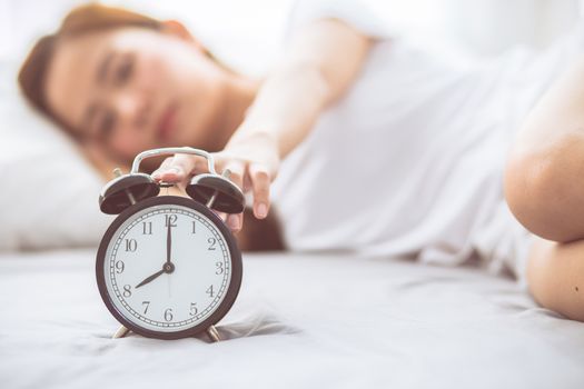 Beautiful asian young woman turn off alarm clock in good morning, wake up for sleep with closeup foreground alarm clock, relax and lifestyle concept.