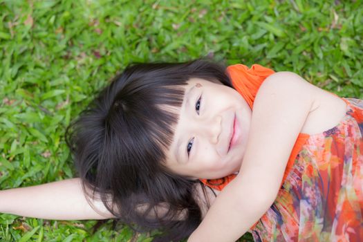 Beautiful portrait little girl asian of a smiling lying on green grass at the park, kid leisure and joyful in outdoor.