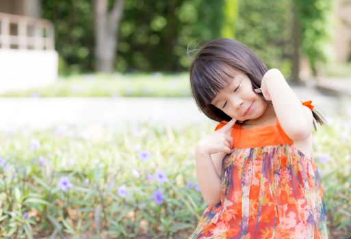 Beautiful portrait little girl asian of a smiling standing on green grass at the park, kid leisure and joyful in outdoor.