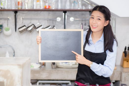 Portrait of beautiful young barista, asian woman is a employee standing holding chalkboard in counter coffee shop, service concept.