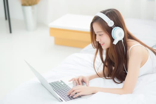 Beautiful asian young woman relax listening to music with headphone and laptop online internet on vacation in bedroom, cheerful of asia girl leisure, lifestyle concept.