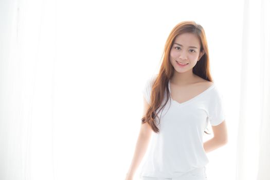Beautiful young asian woman standing the window and smile while wake up with sunrise at morning, lifestyle and relax concept.