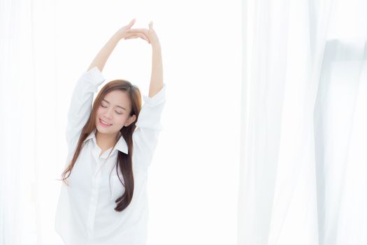 Beautiful young asian woman stretch and relax standing in bed after wake up morning at bedroom, new day and resting for wellness, lifestyle concept.