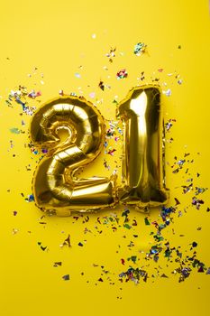 Number 21 from golden foil balloon and confetti on yellow background stock photo