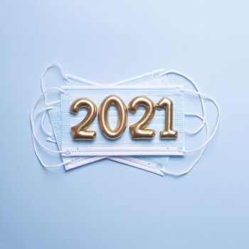 Gold numbers 2021 with face mask on blue background. Happy new pandemic year