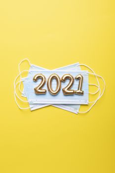 Gold numbers 2021 with face mask on bright yellow background. Happy new pandemic year