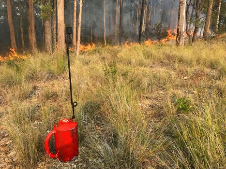A red drip torch with fire in the background