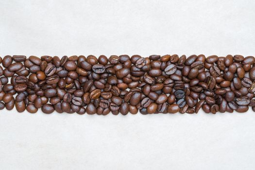 Brown coffee beans on background of light texture recycled eco-friendly paper. Central horizontal location objects, copy space for text at top and bottom. Flat lay, close-up view of still life.