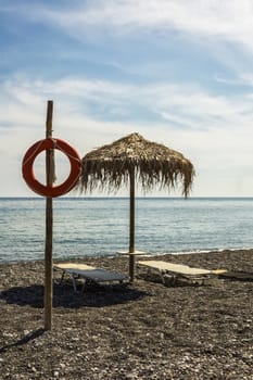 On the beach there is a pole with a lifeline, near an umbrella and two sunbeds.