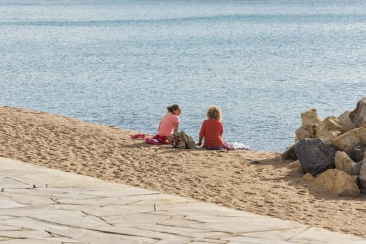 Spain, Blanes - September 16, 2017: Two girls are sitting on the beach near the water and talking