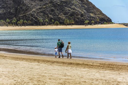Spain, Tenerife - May 07, 2018: A man with a woman and a child walking along a deserted beach near the water