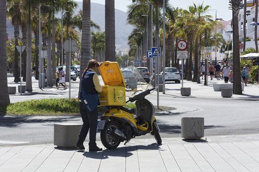 Spain, Tenerife - May 14, 2018: A postman girl stands near a yellow scooter on the sidewalk