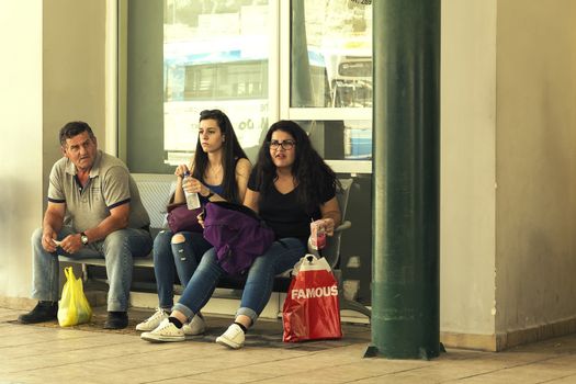 Greece, Zakynthos Island - June 17, 2016: Two young girls and an elderly man sit on a bench in a bus lazy