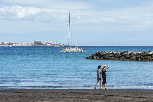 Spain, Tenerife - May 10, 2018: Two young women stroll along the beach near the water