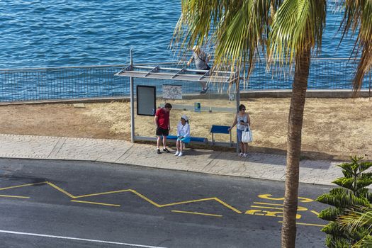 Spain, Tenerife - May 08, 2018: A group of people standing at a public transport stop on the ocean