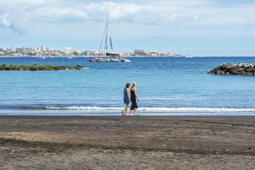 Spain, Tenerife - May 10, 2018: Two young women walk on the beach near the water