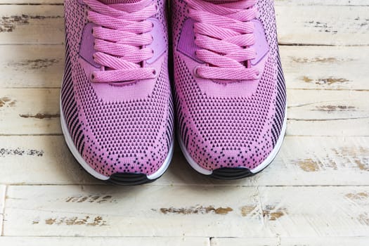 On the wooden surface is a pair of pink sneakers with pink laces
