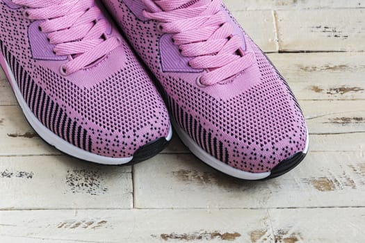 A pair of pink sneakers with pink laces stands on a wooden surface