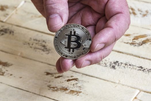 Against the background of the wooden surface of the man's hand holding a silver coin bitcoin