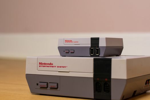 A Nintendo Entertainment System Classic Edition on Top of an Original Nintendo Entertainment System, on a wood floor. Comparison of the original NES against the NES Classic Edition