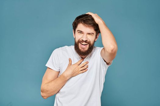 A bearded man in a white T-shirt gestures with his hands emotions blue background. High quality photo