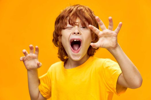 An expressive boy imitates animals and gestures with his hands on a yellow background Copy space