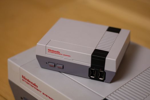 A Nintendo Entertainment System Classic Edition on Top of an Original Nintendo Entertainment System, on a wood floor. Comparison of the original NES against the NES Classic Edition