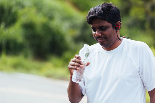 Close up Asian young sport runner black man wear athlete headphones he drinking water from a bottle after running at the outdoor street health park, healthy exercise workout concept