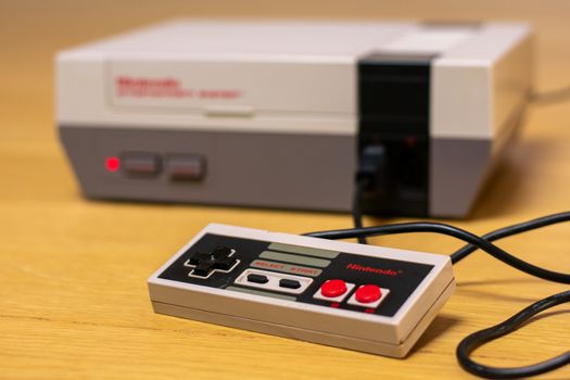 The Controller of a Nintendo Entertainment System on a wooden floor plugged into the console.