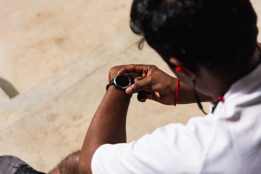 Close up Asian young athlete sport runner black man wear modern time smart watch he sitting resting before training running at the outdoor street health park, healthy exercise before workout concept