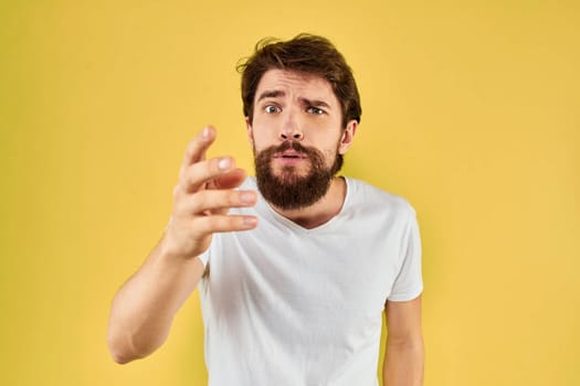 A man in a white t-shirt gestures with his hands lifestyle cropped view yellow background more fun. High quality photo