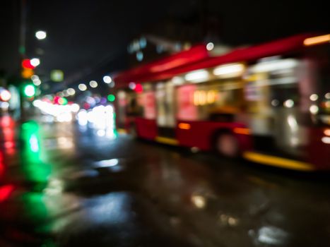 defocused night rain city street view with red bus crossing road with car traffic