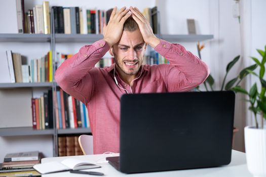 Attractive young man sitting at the table at home working with a laptop feeling worried and frustrated