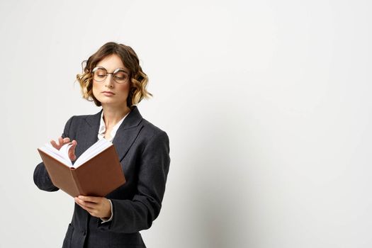 Woman at work with book in hand light background classic suit glasses head. High quality photo