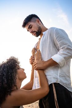 Kneeling submissive woman begs her man by holding his hands on his massive chest, but he squeezes her wrists as a sign of possession and domination - Multiracial lovers couple romance scene