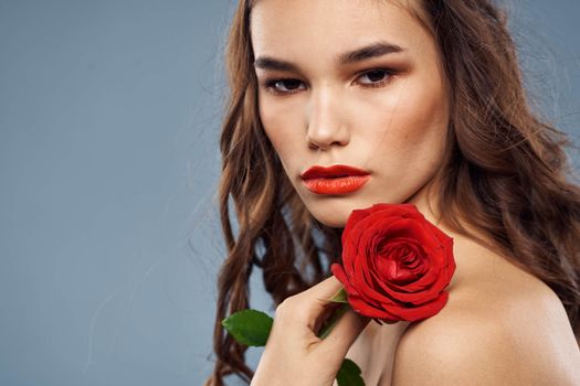 Woman portrait with red rose near the face on gray background and makeup curly hair. High quality photo