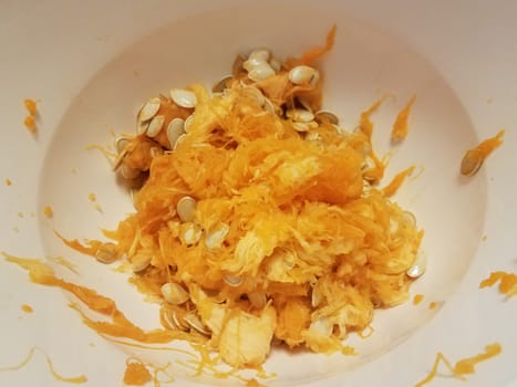 pumpkin seeds and orange pulp in white container