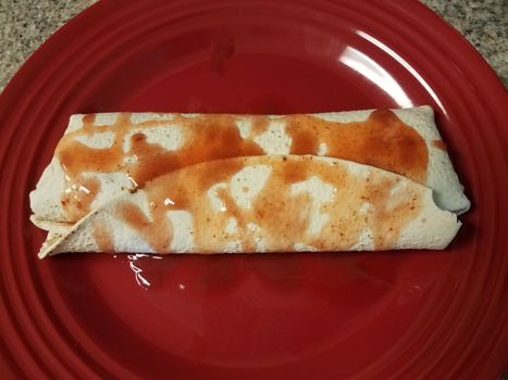 spicy red salsa on burrito on red plate