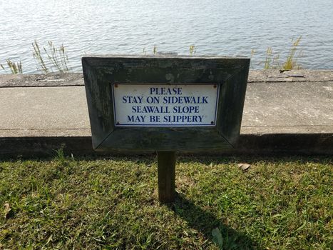 seawall slope may be slippery sign near water with sidewalk