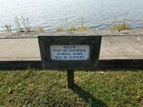 seawall slope may be slippery sign near water with sidewalk