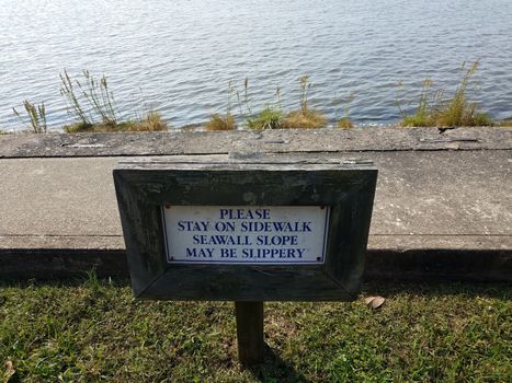 seawall slope may be slippery sign near water with sidewalk