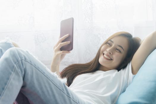 Attractive smiling asian woman using smart phone on the relaxing sofa at home. Relaxation and Stay at home.