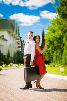 Young couple of criminals with weapons and a suitcase full of money.