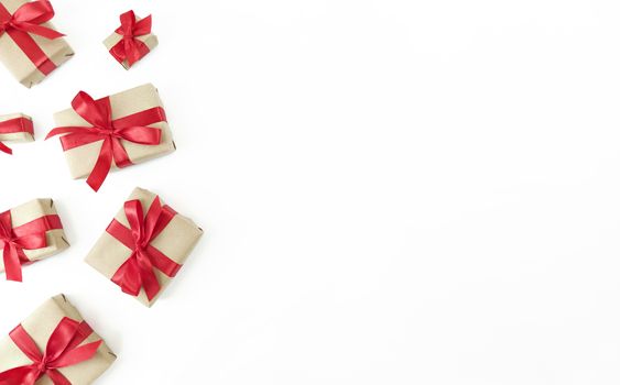 Gift boxes wrapped in craft paper with red ribbons and bows on white background. Festive flat lay with copy space.