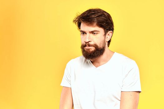 Bearded man in a white T-shirt gestures with his hands emotions studio yellow background. High quality photo