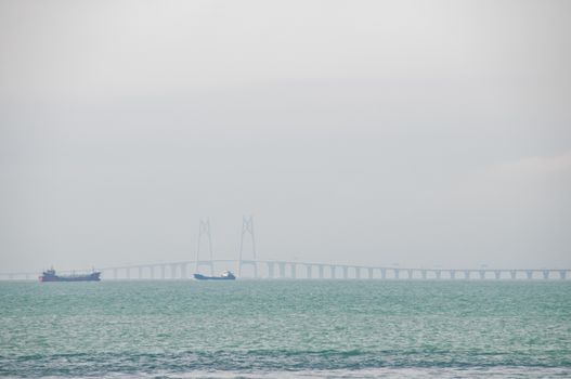 HONG KONG, HONG KONG SAR - NOVEMBER 18, 2018: Zuhai giantic mega bridge between China mainland and Hong Kong island. There are 2 ships floating near the bridge in hazy afternoon.